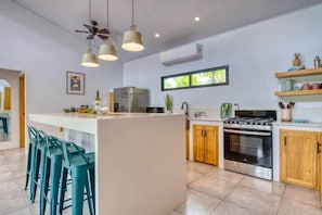 A modern kitchen with a central island, bar stools, a stove, and a refrigerator. - Villa Casa Tangerine with Private Pool (Sámara)