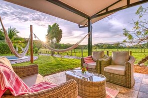 A covered outdoor seating area with wicker furniture, a hammock, and a view of a lush landscape.
