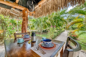 Un espacio al aire libre para comer con una mesa de madera dispuesta para dos personas, rodeado de exuberante vegetación tropical.