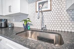 A kitchen with a stainless steel sink, a toaster, a potted plant, and a framed picture on the wall. - Modern Comfort Belmar Lofts Apartment C Lk Hollingsworth 2 King Suites (Lakeland)