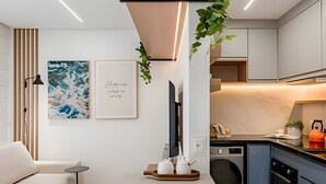 Une cuisine moderne équipée d’un four encastré, d’un lave-linge et d’un coin repas avec une table blanche et un canapé.