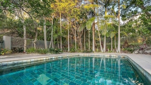 Una piscina con acqua cristallina blu, circondata da diversi alberi e una recinzione metallica.