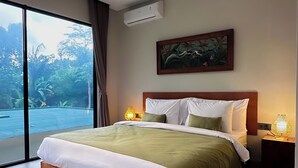 A modern bedroom with a large bed, a painting above the bed, and a view of a swimming pool through the window. - Marvelous 3-bedroom villa with AC in vibrant Ubud Bali (Bali)