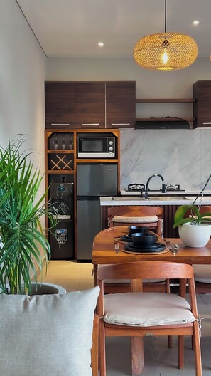 Une cuisine moderne équipée d’un four à micro-ondes encastré, d’un réfrigérateur et d’une cuisinière à gaz. On y trouve une table à manger avec des chaises et un luminaire suspendu au-dessus.