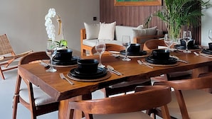 A modern dining area with a wooden table set for four, surrounded by chairs. There are three hanging wicker lamps above the table, and a large painting of flowers on the wall behind the seating area. - Marvelous 3-bedroom villa with AC in vibrant Ubud Bali (Bali)