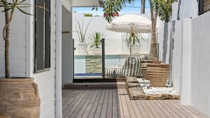 A wooden deck with potted plants, a striped cushion, and a white umbrella.