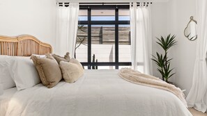 Ein Schlafzimmer mit einem großen Bett, weißer Bettwäsche und Meerblick durch ein großes Fenster.