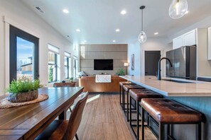 A modern kitchen with a central island, bar stools, and a large TV. - Teton Homestead: Teton Timber Retreat | Hot Tub (Driggs)