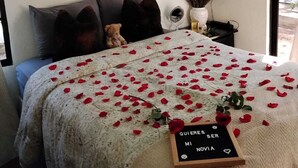 A bedroom with a bed covered in rose petals, a decorative tree on the wall, and a sign with a message.