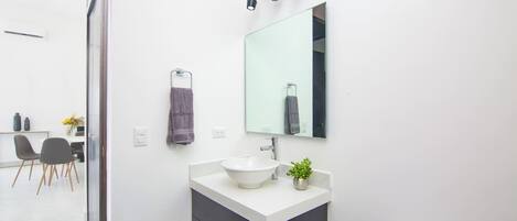 A modern bathroom with a white sink, black cabinet, and a large mirror. There is a small plant on the sink counter and a towel hanging on a rack.