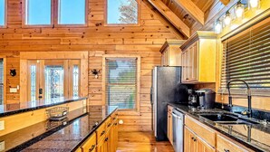 A wooden cabin interior with a kitchen featuring wooden cabinets, a granite countertop, and a large refrigerator. - Luxe Sister Cabins, Sleeps 24, Pool, Hot Tub, Games (Gatlinburg)