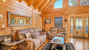 A cozy log cabin interior with a wooden ceiling, a large mirror, a sofa, a chair, and a coffee table. - Luxe Sister Cabins, Sleeps 24, Pool, Hot Tub, Games (Gatlinburg)