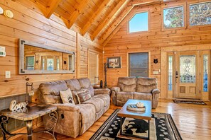 Ein gemütliches Blockhaus-Interieur mit Holzboden, einem großen Spiegel, einer Couch, einem Sessel und einem Couchtisch.