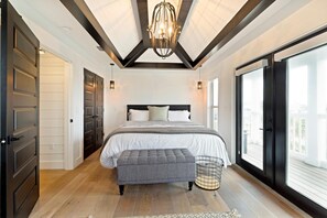 Un dormitorio con una cama grande, un banco, una araña y vistas a través de un puertas correderas.