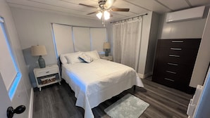 A bedroom with a bed, nightstands, a dresser, a ceiling fan, and a window with curtains.