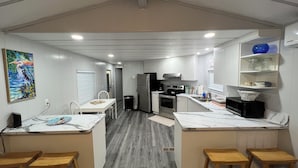 A modern kitchen with white cabinets, a stainless steel refrigerator, a microwave, and a sink. There are wooden stools and a table with a white tablecloth.