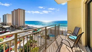 A balcony with a view of the ocean and beach, a pool, and a cityscape in the background. - Origin 0933 - Studio King - Gulf View (Panama City Beach)