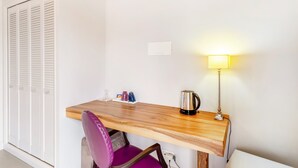 Een kamer met een houten bureau, een paarse stoel, een lamp, een waterkoker en een witte garderobe.