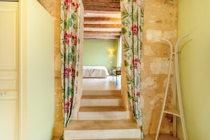 A staircase with floral curtains, a bed in the background, and a white ladder.