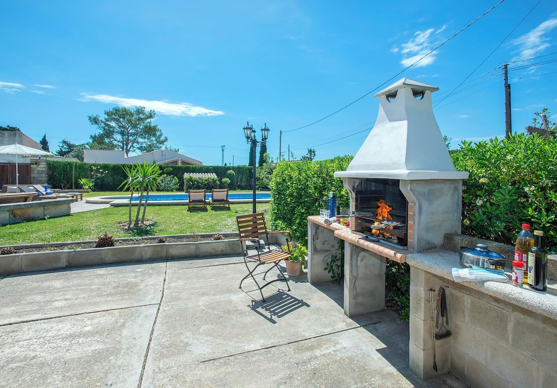 An outdoor barbecue area with a stone grill, a pool, and a lawn.