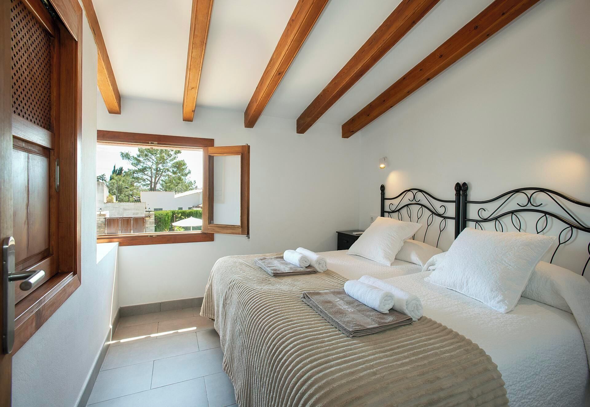 A bedroom with a bed, two pillows, a nightstand, a window, and wooden beams on the ceiling.