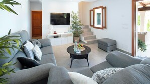 Ein modernes Wohnzimmer mit grauen Sofas, einem Flachbildfernseher, einem Couchtisch mit Früchten und einer Treppe.
