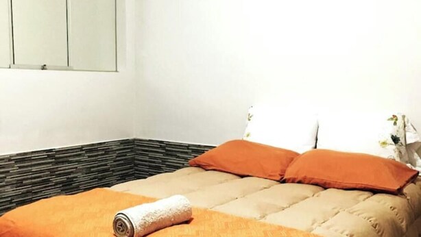A bed with orange bedding, a rolled towel, and a wall with a patterned design. - Fenced apartment (additional garage) (San Salvador)