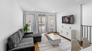 A modern living room with a grey sectional sofa, a white coffee table, and a TV mounted on the wall. - 3BR Apt Mins to Bus, Newark Airport, Penn Sta, NYC (Newark)