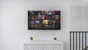 A wall-mounted TV displaying various movie and TV show posters. Below the TV, there is a white cabinet with geometric patterns and gold handles. - 3BR Apt Mins to Bus, Newark Airport, Penn Sta, NYC (Newark)