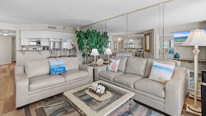Un salon moderne avec un canapé beige, une table basse en verre et une grande plante.