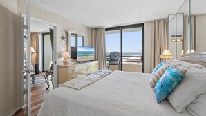 Une chambre d’hôtel avec un grand lit, une télévision, un bureau avec une lampe et une vue sur la mer par la fenêtre.