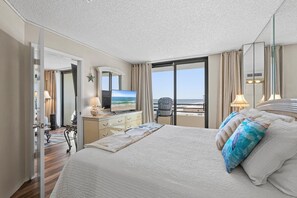 Une chambre d’hôtel avec un grand lit, une télévision, un bureau avec une lampe et une vue sur la mer par la fenêtre.