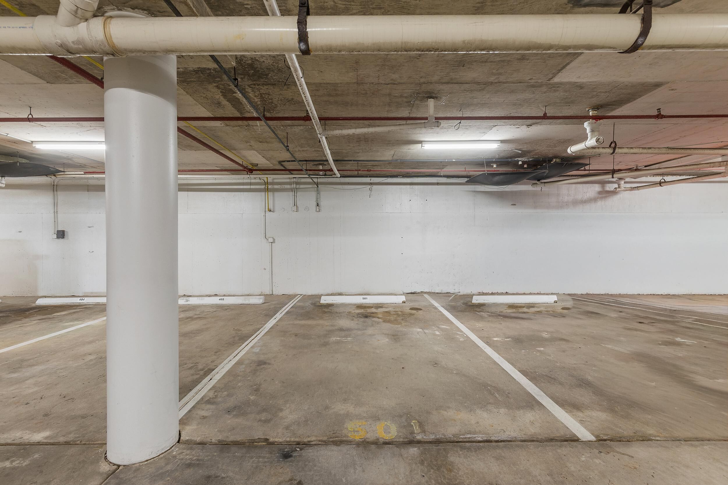 An empty parking garage with concrete floors, white pillars, and visible pipes on the ceiling.