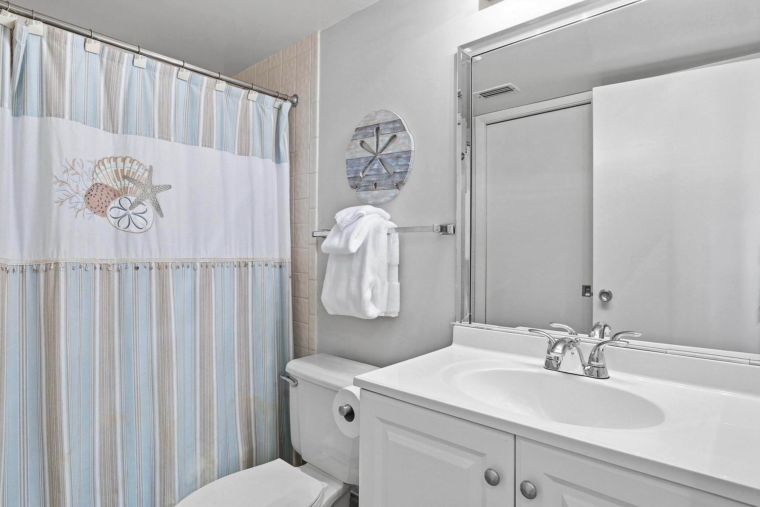 A bathroom with a striped shower curtain, a toilet, a sink with a mirror, and a towel hanging on the wall.