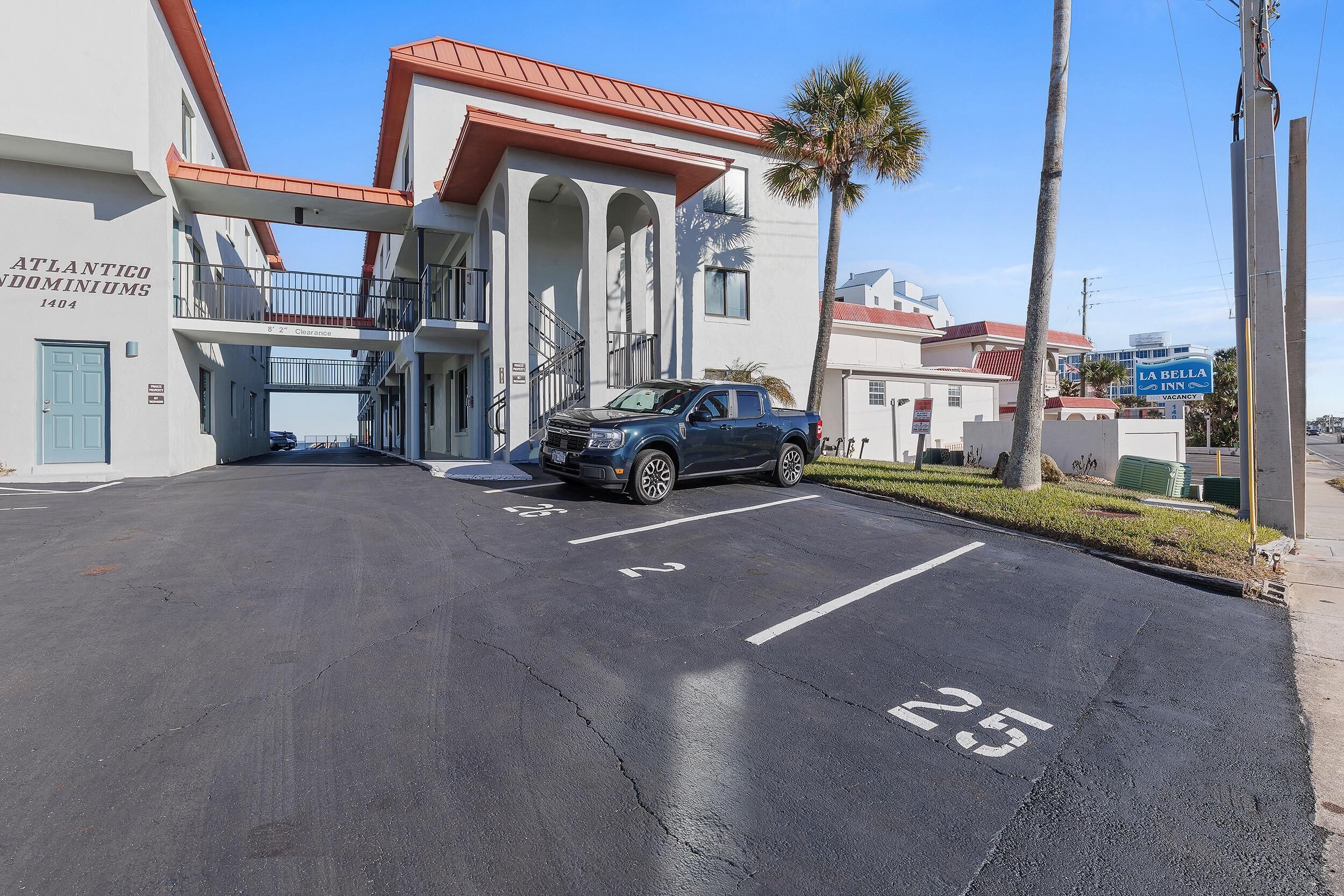 A parking lot with a blue truck, a building labeled "ATLANTICO DORMINIUMS," and a sign for "LA BELLA INN."