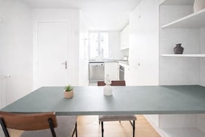 Ett modernt kök med vita skåp, en grå bänkskiva och en matplats med ett bord och stolar.