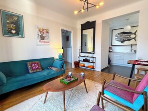 A living room with a teal sofa, a wooden coffee table, and a kitchen area visible through an open doorway. - Le Penthouse Murat C (Paris 16)
