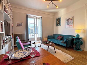 A cozy living room with a wooden dining table, a teal sofa, and a bookshelf filled with books. - Le Penthouse Murat C (Paris 16)