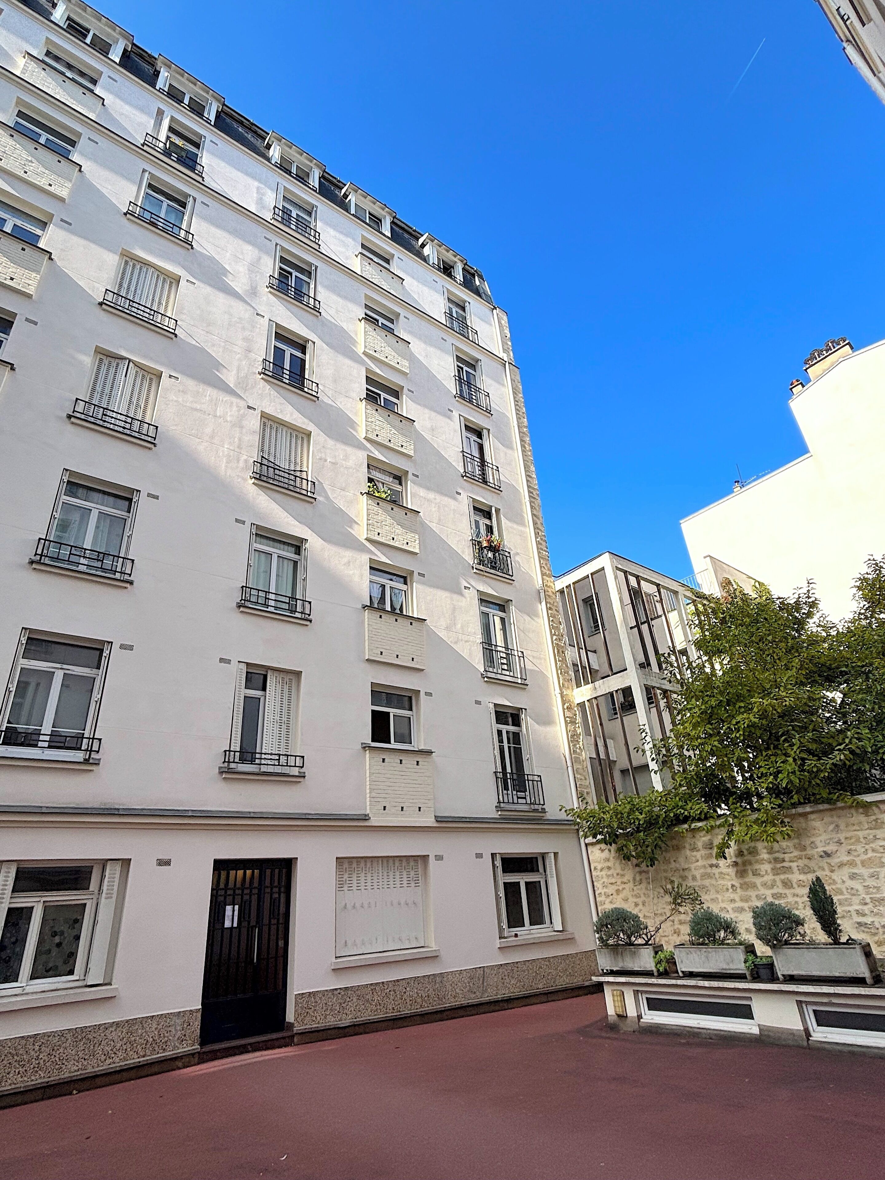 A multi-story residential building with balconies, a red ground floor, and a clear blue sky.