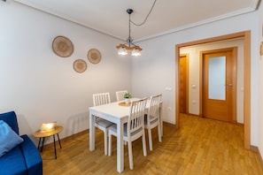 Ein Essbereich mit einem weißen Tisch und Stühlen, einem kleinen Beistelltisch mit Lampe und Holzboden.