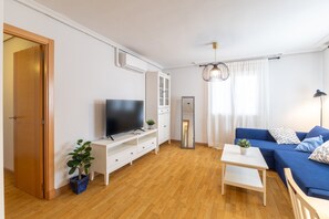 Ein modernes Wohnzimmer mit Fernseher, Sofa, Couchtisch und einer Pflanze.