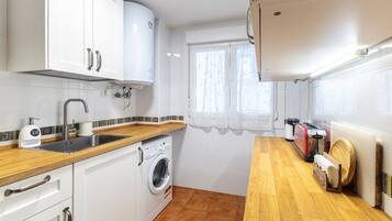 Een kleine keuken met witte kasten, een wasmachine, een spoelbak en een houten aanrecht.