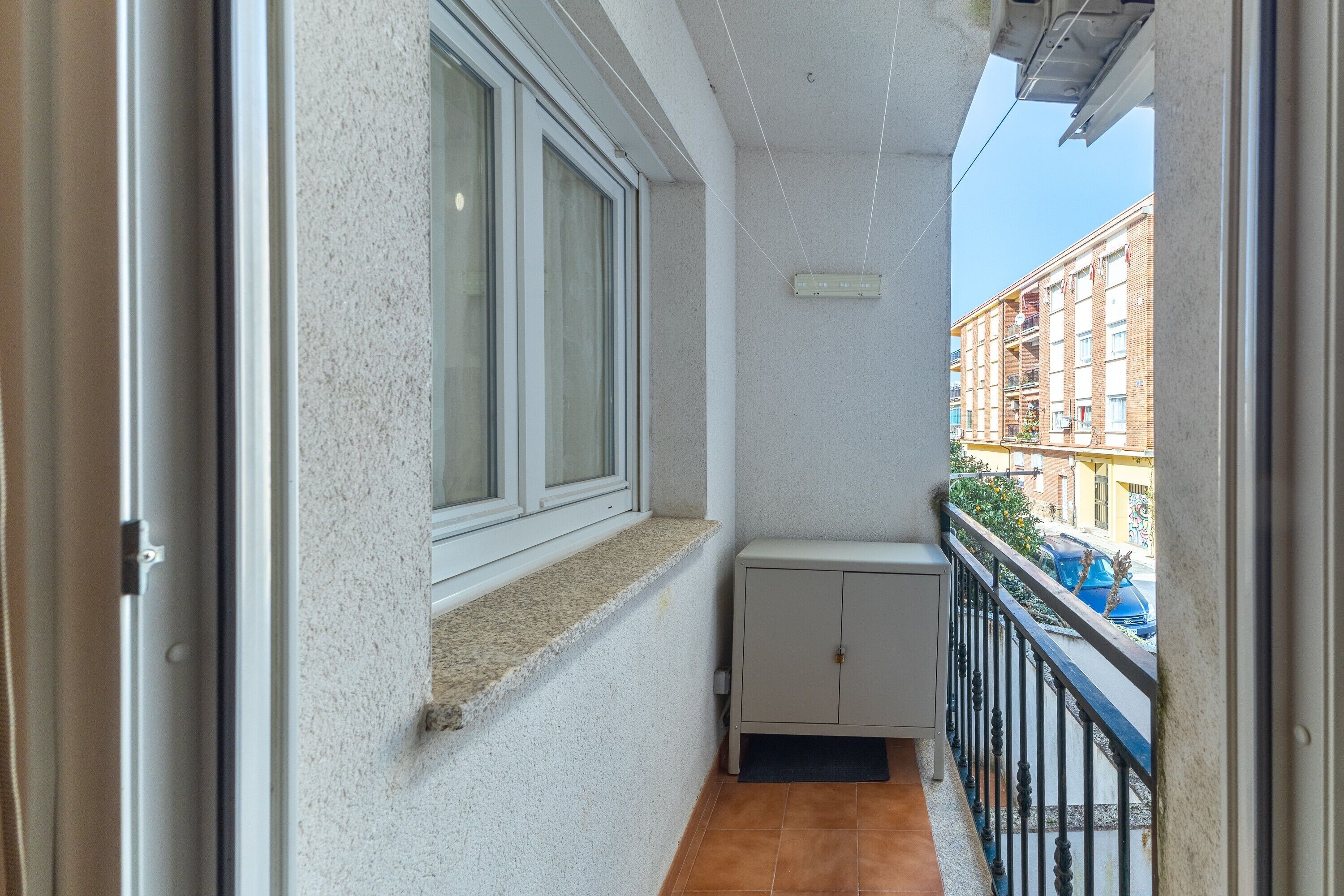 Un balcon étroit avec une fenêtre, un petit placard et une vue sur un immeuble situé de l’autre côté de la rue.