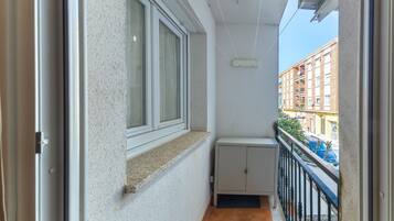 Un balcon étroit avec une fenêtre, un petit placard et une vue sur un immeuble situé de l’autre côté de la rue.