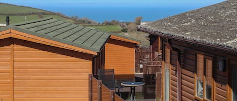 A wooden cabin with a view of the sea, a small outdoor table, and a car parked nearby.