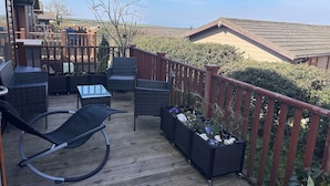 A deck with wicker furniture, a glass table, and planters with flowers. - 1 Ocean Terrace (Ilfracombe)