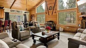 Een gezellig interieur van een chalet met een eethoek, zitplaatsen en grote ramen met uitzicht op het bos.
