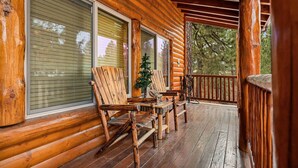 Een houten veranda met een tafel en stoelen, een kleine kerstboom, en een uitzicht op bomen in de achtergrond.