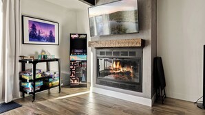 Una sala de estar con chimenea, televisor montado y consola de videojuegos.