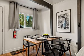 Un comedor con una mesa de madera, sillas negras, un extintor y un cuadro en la pared.